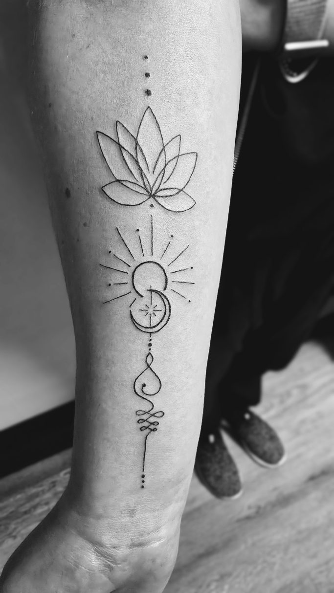 Lotusblume über einem geschwungenen Symbol, Sonne und Mond auf dem Unterarm.