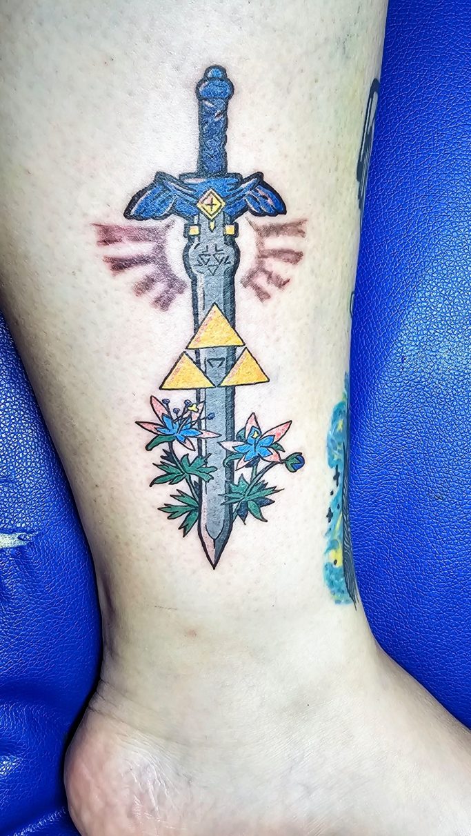 Tattoo eines Schwertes mit einer gemusterten Klinge und dem Triforce-Symbol.
